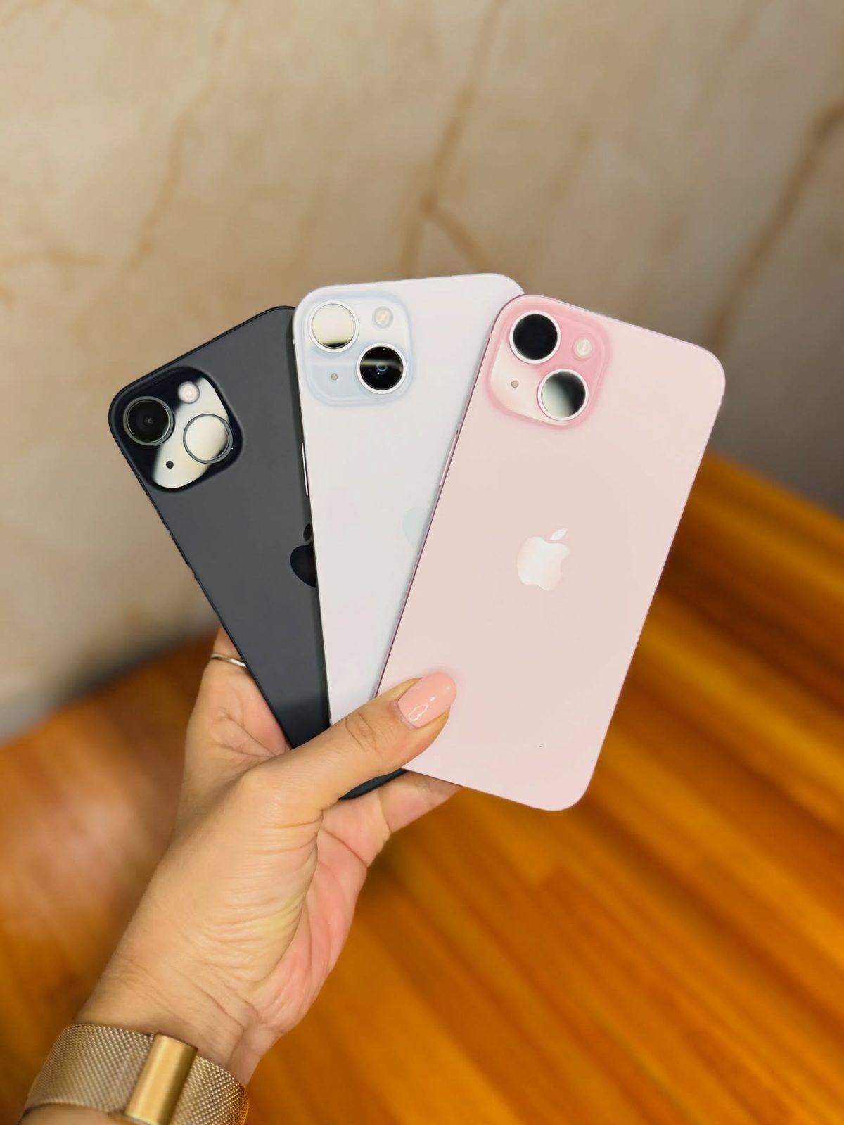 Three iPhone 15 colours held in hand showing camera design - Legacy Luxury Store Ghana